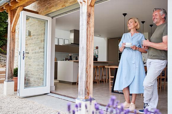 Couple enjoying coffee on a patio with an open door leading to a modern kitchen.
