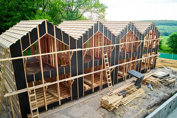 Newly constructed residential houses in framing stage with surrounding greenery.