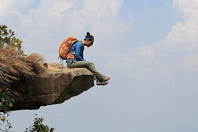 Person sitting on a cliff ledge with a backpack, looking at the horizon.