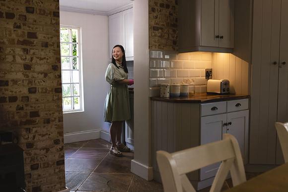 Smiling woman standing in a bright kitchen near a countertop and window.