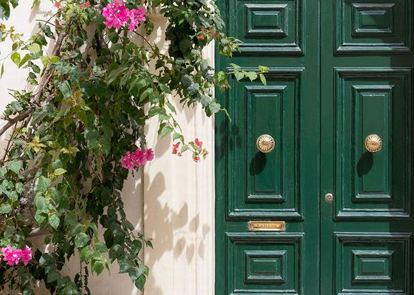 Green double doors adorned with pink flowers and greenery.